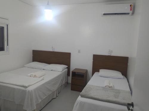 a room with two beds and a nightstand between them at Trentino 66 - Hospedagem em Ijuí, casa agradável com estacionamento in Ijuí