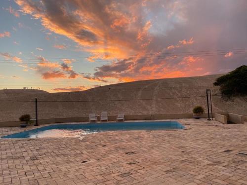 a swimming pool with two chairs and a sunset at Via Praia Apart Hotel in Florianópolis