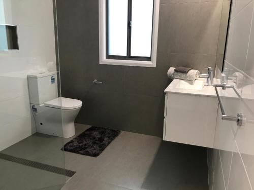 a bathroom with a toilet and a sink and a window at Sunnyside Retreat - Holiday Home - Walk to Nobbys or Flynns Beach , enjoy the sound of waves and birds in Port Macquarie
