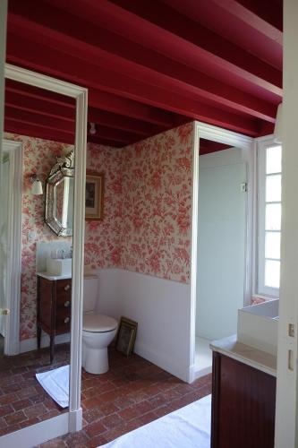baño con aseo y techo rojo en les chambres de la tour, en Le Bec-Hellouin