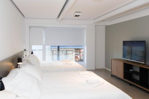 a bedroom with two white beds and a flat screen tv at Austral Departamentos in Ushuaia