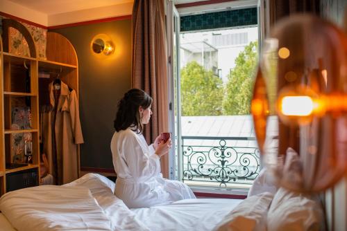 a woman sitting on a bed looking at her cell phone at Hôtel Jardin de Cluny in Paris