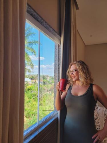 a woman is holding a cup in front of a window at Hotel Encanto do Sertão in Triunfo
