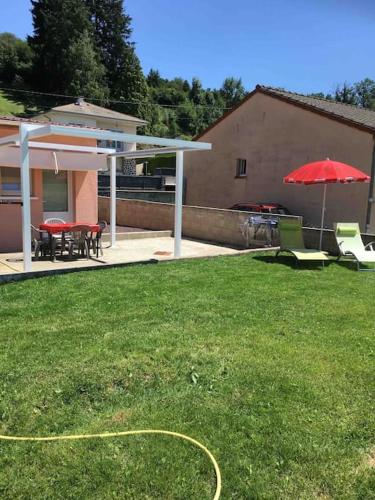 - une cour avec un parasol rouge, des tables et des chaises dans l'établissement Le Coin Tranquille au pied du Puy de Dôme, à Pontgibaud