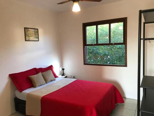 1 dormitorio con 1 cama con manta roja y ventana en Apartamento do Norte na Ferrugem en Garopaba
