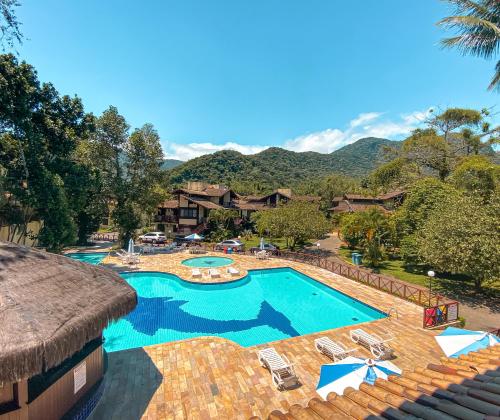 a resort with a pool and chairs and mountains in the background at Flat 1 Dorm. Maresias Praia&Lazer& Ar&Piscina F3 in São Sebastião