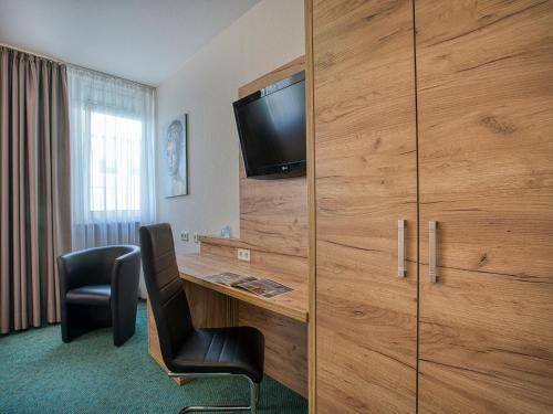 a hotel room with a desk and a tv on a wall at Centro Hotel Böblingen, Trademark Collection by Wyndham in Böblingen