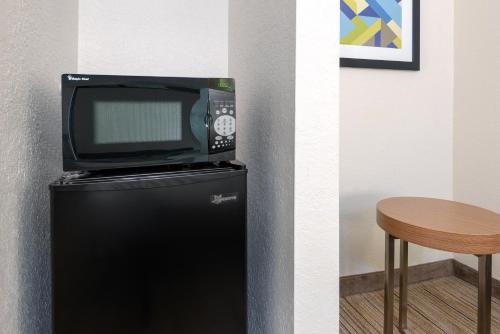 a television on top of a refrigerator next to a table at Holiday Inn Express Hotel & Suites Bonita Springs/Naples by IHG in Bonita Springs