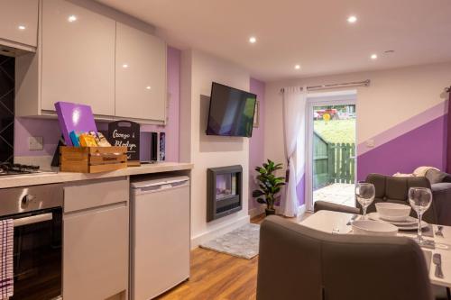 a kitchen and living room with purple walls and a table at Blodyn Cottage - Cosy, Self-Catering with Private Hot Tub in Bodfari