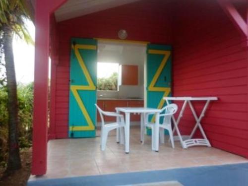 a red house with two tables and chairs on a porch at Maison charmante à Sainte-Rose, piscine. in Sainte-Rose