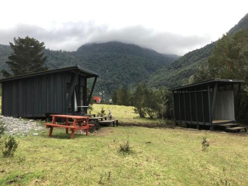 a picnic table and a bench in a field with mountains at Base Puelo in Cochamó