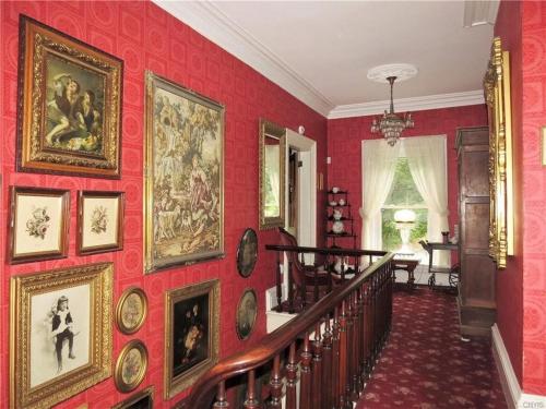 a hallway with a bunch of paintings on a red wall at Raindrops On Roses Bed & Breakfast in Herkimer