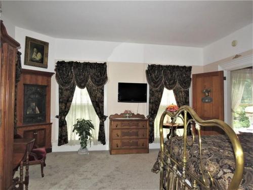 a bedroom with a bed and a tv and curtains at Raindrops On Roses Bed & Breakfast in Herkimer