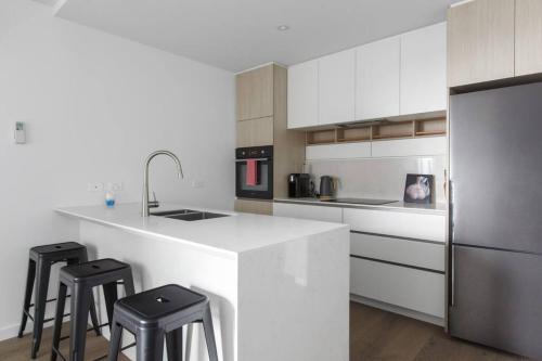 a kitchen with a white counter and two stools at Resort Style Living In the Heart of Moonee Ponds in Melbourne