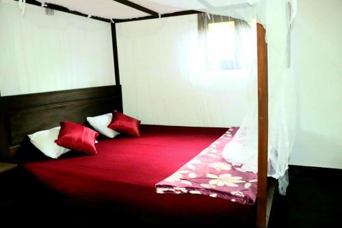 a bed with red sheets and pillows in a room at Rainforest River Bay in Deniyaya