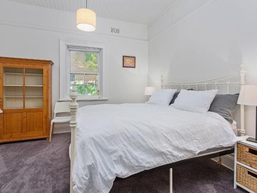 a white bedroom with a white bed and a window at Merioola Retreat in Gerringong