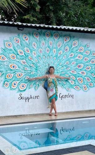 a woman standing in front of a wall with a peacock painting at Sapphire Garden Hotel in Habarana