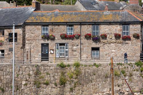 an old stone building with flowers on the windows at The Ship Inn in Mousehole