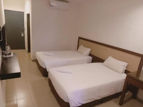 two beds in a hotel room with white sheets at T Hotel Anggerik in Alor Setar