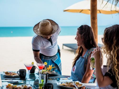 a group of people sitting at a table with food at Maalu Maalu Resort & Spa - Thema Collection in Pasikuda