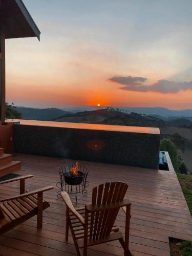 a deck with two chairs and a fire pit with the sunset at Quinta dos Pinhais Pouso e Charme in Santo Antônio do Pinhal