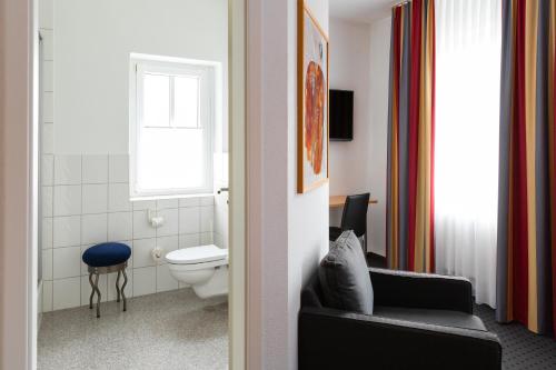 a bathroom with a toilet and a chair and a window at Tiemanns Boardinghouse in Lemförde