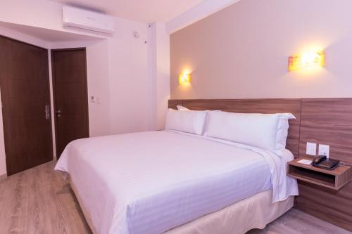 a bedroom with a large white bed with a wooden headboard at Crown Victoria Hotel in Querétaro