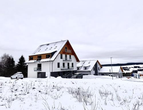 a white house in a snow covered field with cars at Apartmány na Plešivci in Abertamy