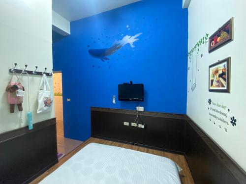 a room with a blue wall with a bed and a tv at Danke Hostel in Xiaoliuqiu