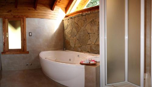 a bathroom with a tub and a stone wall at Tillka - Casas de Montaña in Villa La Angostura