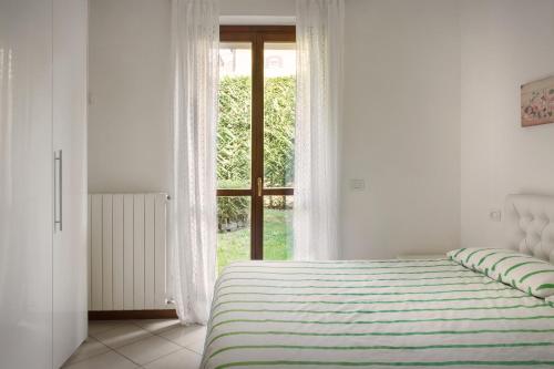 a white bedroom with a bed and a window at Casa Cariza-Appartamento con piscina in Colà di Lazise