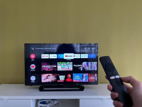 a person holding a remote control in front of a tv at Sky Bungalow NIlai by James NEARBY KLIA, KLIA 2, CYBERJAYA, PUTRAJAYA in Nilai