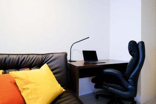 a desk with a laptop and a leather chair at ケイアイコンホテルズ ふくしあ503 in Chikusachō