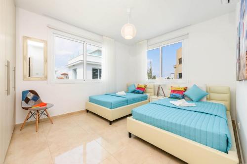 a bedroom with two beds and a chair and windows at Green Bay Villa #13 in Protaras