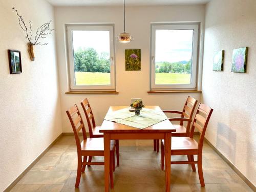 a dining room with a table and chairs and two windows at Haus Sonnentau Wohnung 2 in Kißlegg