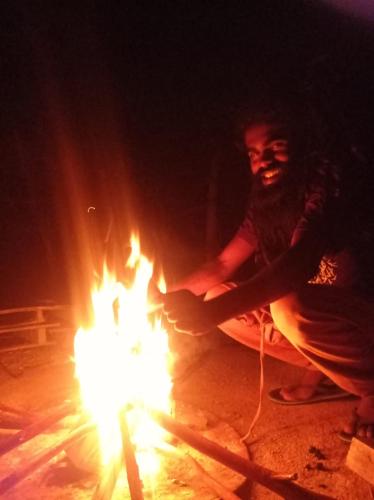 a man is sitting next to a fire at Freedom camp & cafe ella in Ella