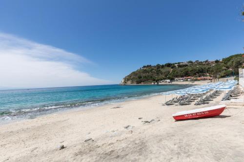 a beach with chairs and a red boat on it at Villaggio Baia D'Ercole in Capo Vaticano