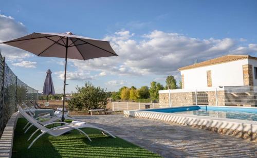 ein Paar Stühle und ein Regenschirm neben einem Pool in der Unterkunft Alojamiento rural La Granja de Las Monjas in Jaén