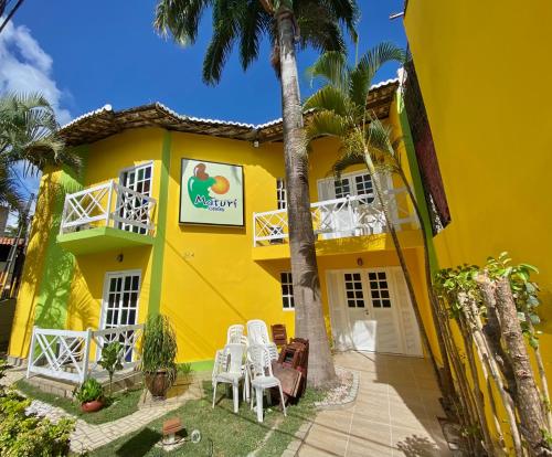 une maison jaune avec des chaises blanches et des palmiers dans l'établissement MATURI CENTRO, à Pipa