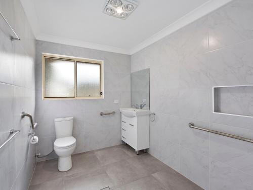 a white bathroom with a toilet and a window at Bonnieview House in Shelly Beach