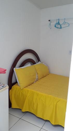 a bed with yellow sheets and a wooden headboard at Suíte 1 Zona Sul Ilhéus próximo a praia in Ilhéus