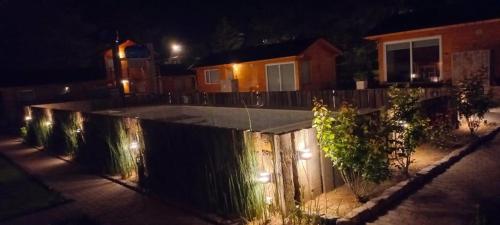 un patio trasero por la noche con una valla con luces en Cabañas Boutique Los Cipreses en Villa Ventana