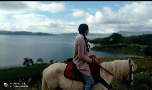 a woman riding a white horse near a lake at Cabañas el Olimpo in Aquitania