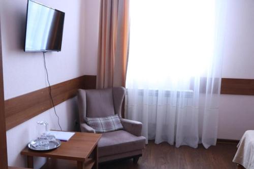 a room with a chair and a table and a television at Hotel Kameliya-v in Vladikavkaz