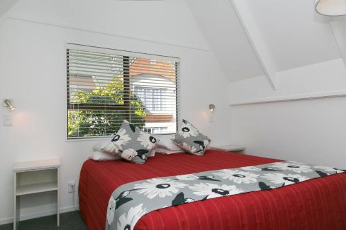 a bedroom with a bed with a red blanket and a window at Gables Lakefront Resort in Taupo