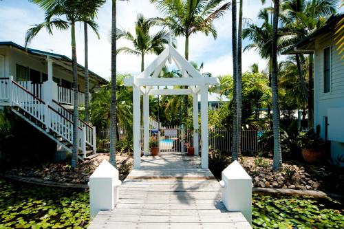 a white archway leading to a house with palm trees at Mango House Resort in Airlie Beach