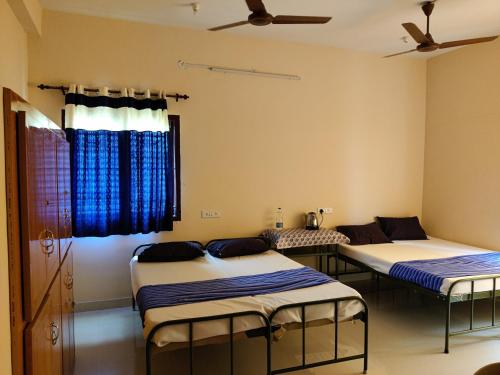3 camas en una habitación con cortinas azules en Sundaram Rooms en Coimbatore