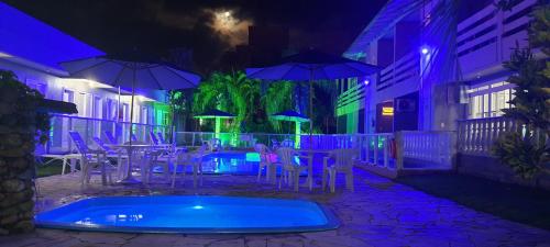 a patio with tables and chairs and a swimming pool at night at Hotel Pousada Ilha do Mar Bombinhas in Bombinhas