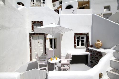 a white patio with a table and an umbrella at Oia Mare Villas in Oia