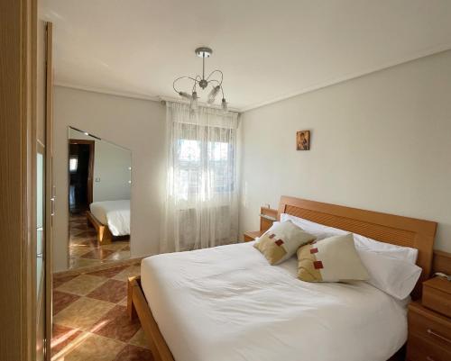 um quarto com uma cama com lençóis brancos e um espelho em CÓMODO alojamiento en Alba de Tormes em Alba de Tormes